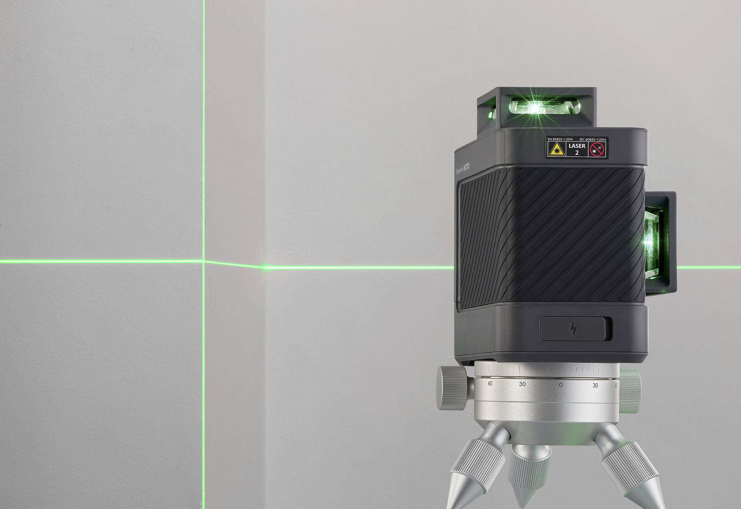 A laser level projects green lines onto the wall, helping with alignment and measurement. The device is mounted on a tripod.