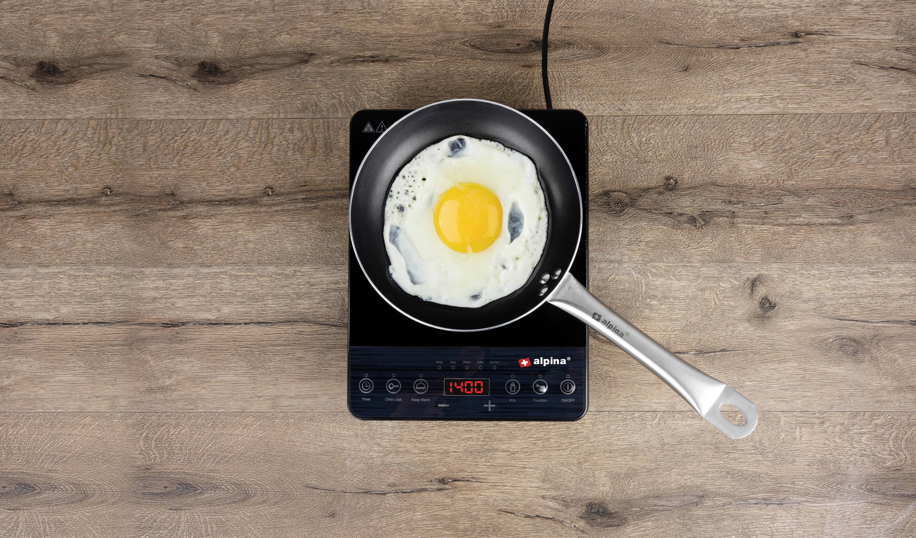 A fried egg in a pan on an activated induction hob. The digital display shows '1400'.