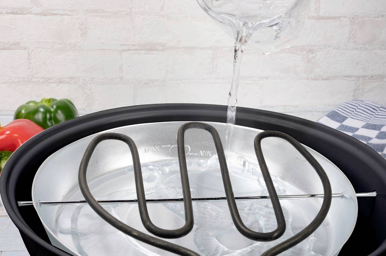 'A steamer is filled with water. Peppers and a tea towel are visible in the background.'