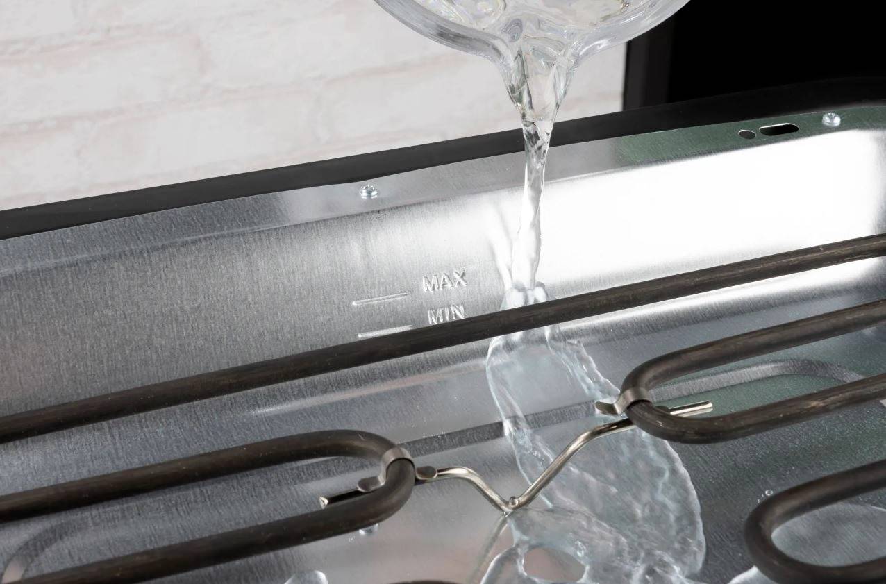 Water is poured into the water tank of a metallic device until the 'MAX' marking is reached. Heating elements visible.