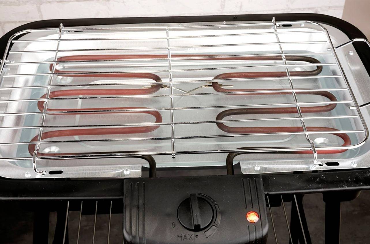 Electric table-top grill with heating coils and temperature control, ready for grilling; red indicator light shows operation.