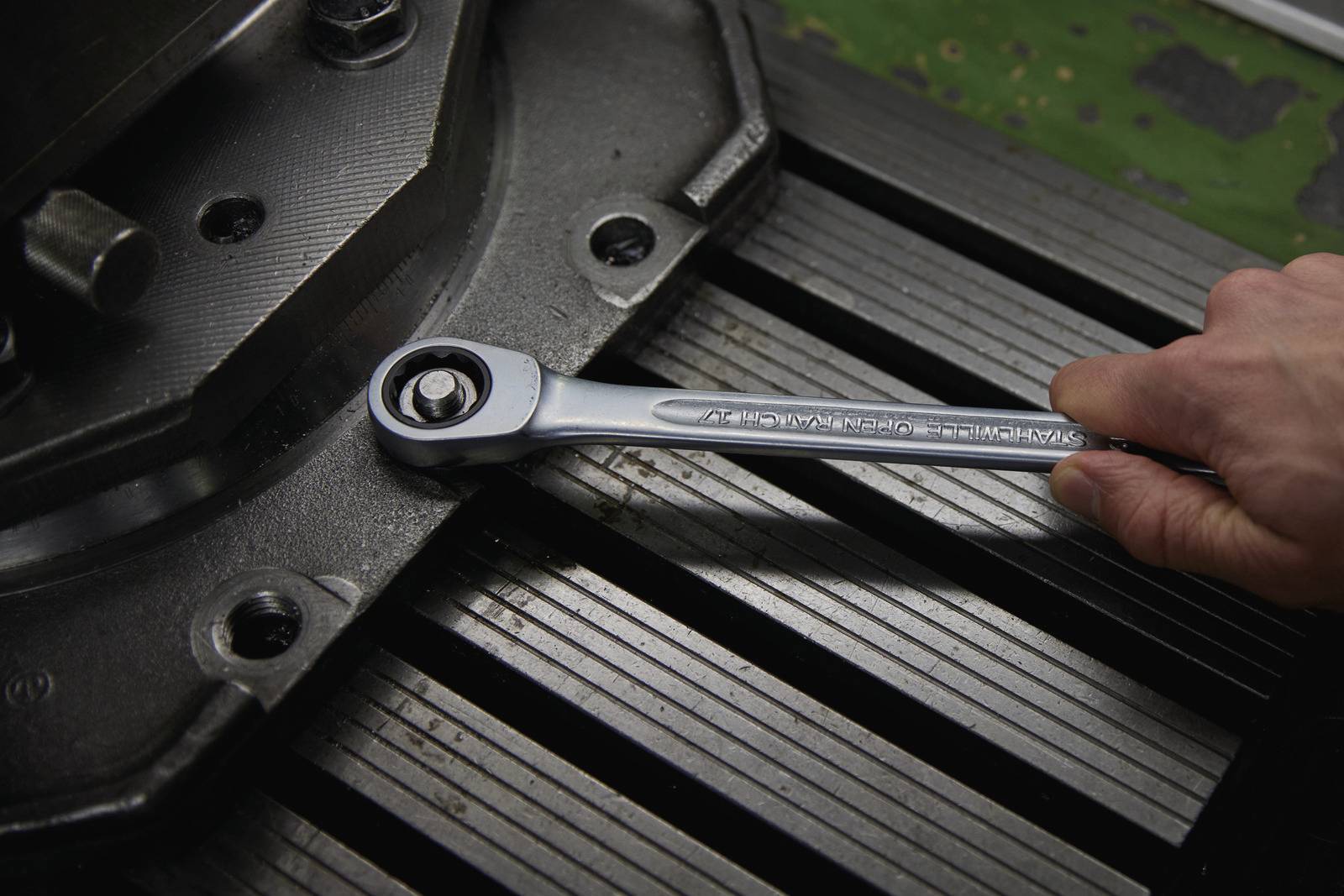 'A hand tightens a screw on a metal plate using a spanner.'<br><br>Note: In British English, a "spanner" is used instead of the American "wrench", while maintaining the precise meaning of the original German sentence.