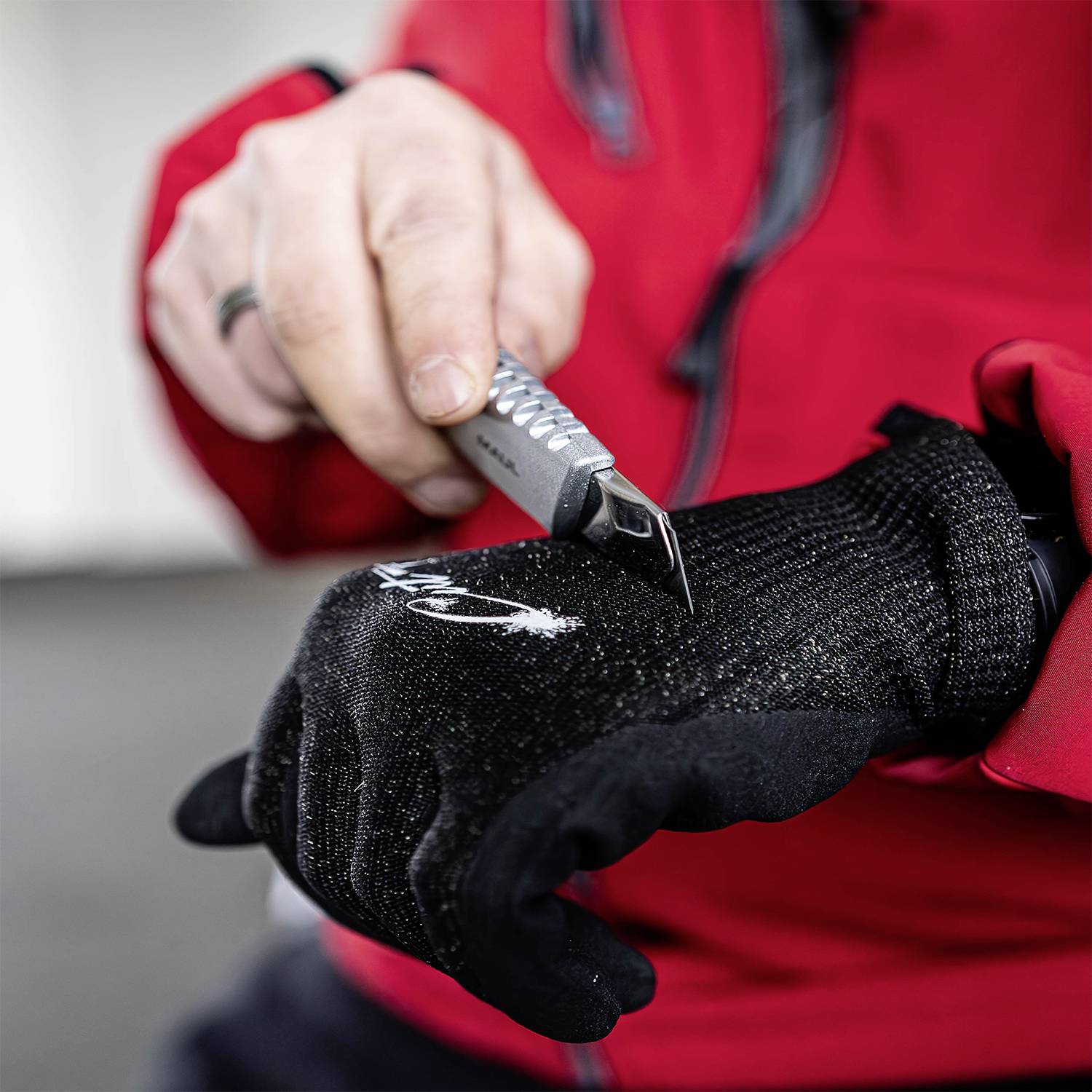 A person in a red jacket is sharpening a knife with a grinding tool against a black, roughly textured surface.