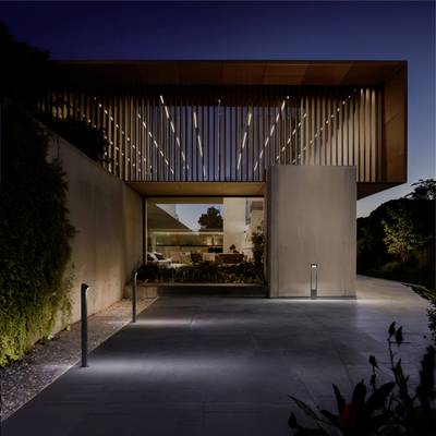 A modern house at dusk with slatted wood design and warm lighting, surrounded by greenery. Minimalist architecture with large windows.