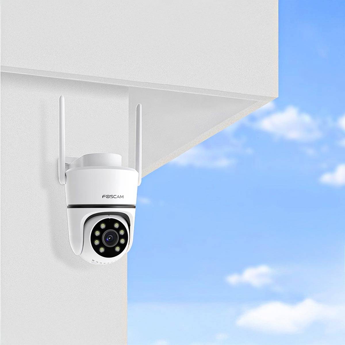 Security camera mounted on a wall, view of blue sky with clouds in the background.
