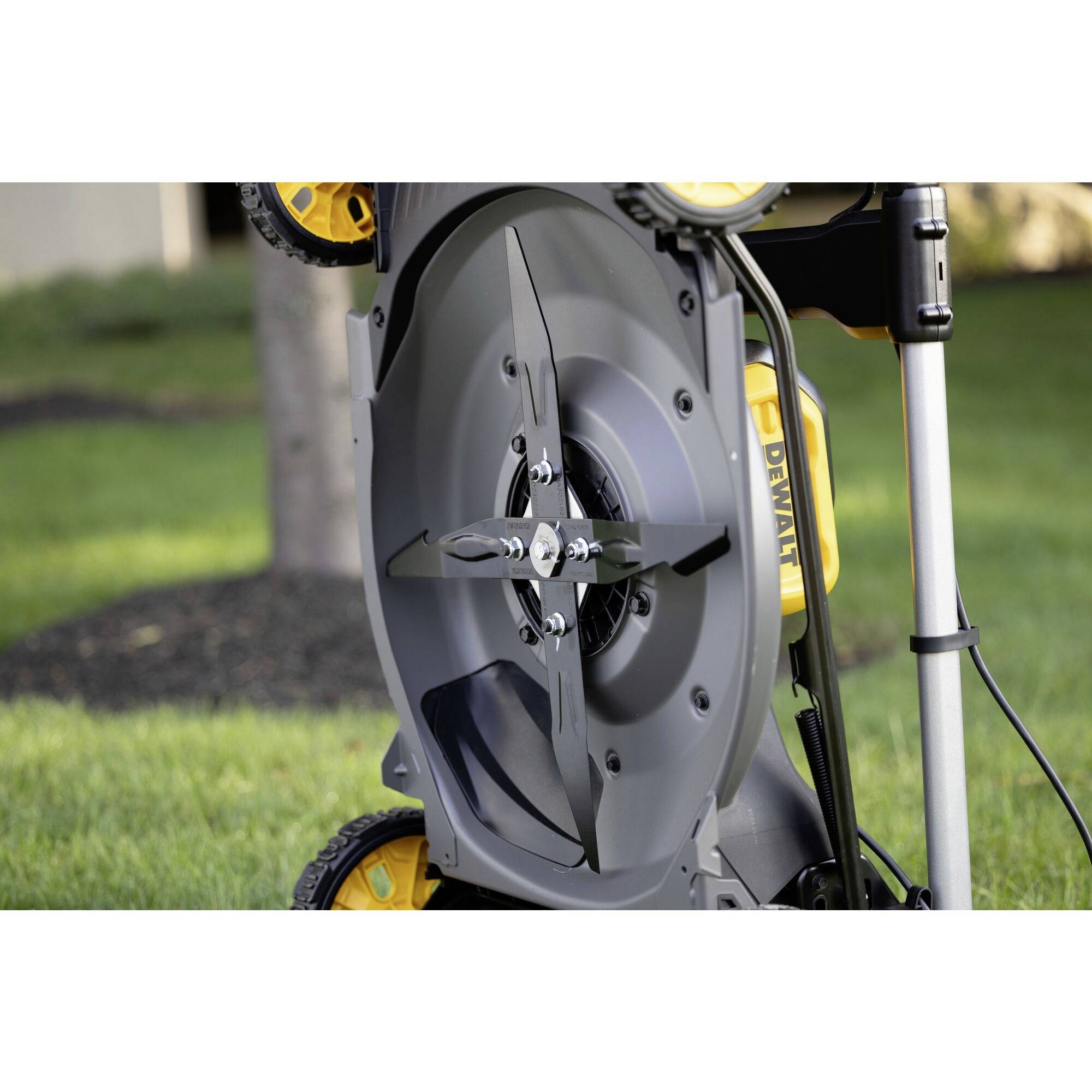 'Close-up of a vertically positioned lawn mower underside with two sharp blades in a garden.'