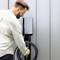 A man is plugging a charging cable into an electric vehicle charging station on a wall. The reception area is designed in a modern style.