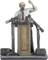 A miniature figurine stands behind a lectern, surrounded by microphones. The figure holds a fist in the air as if delivering a speech.