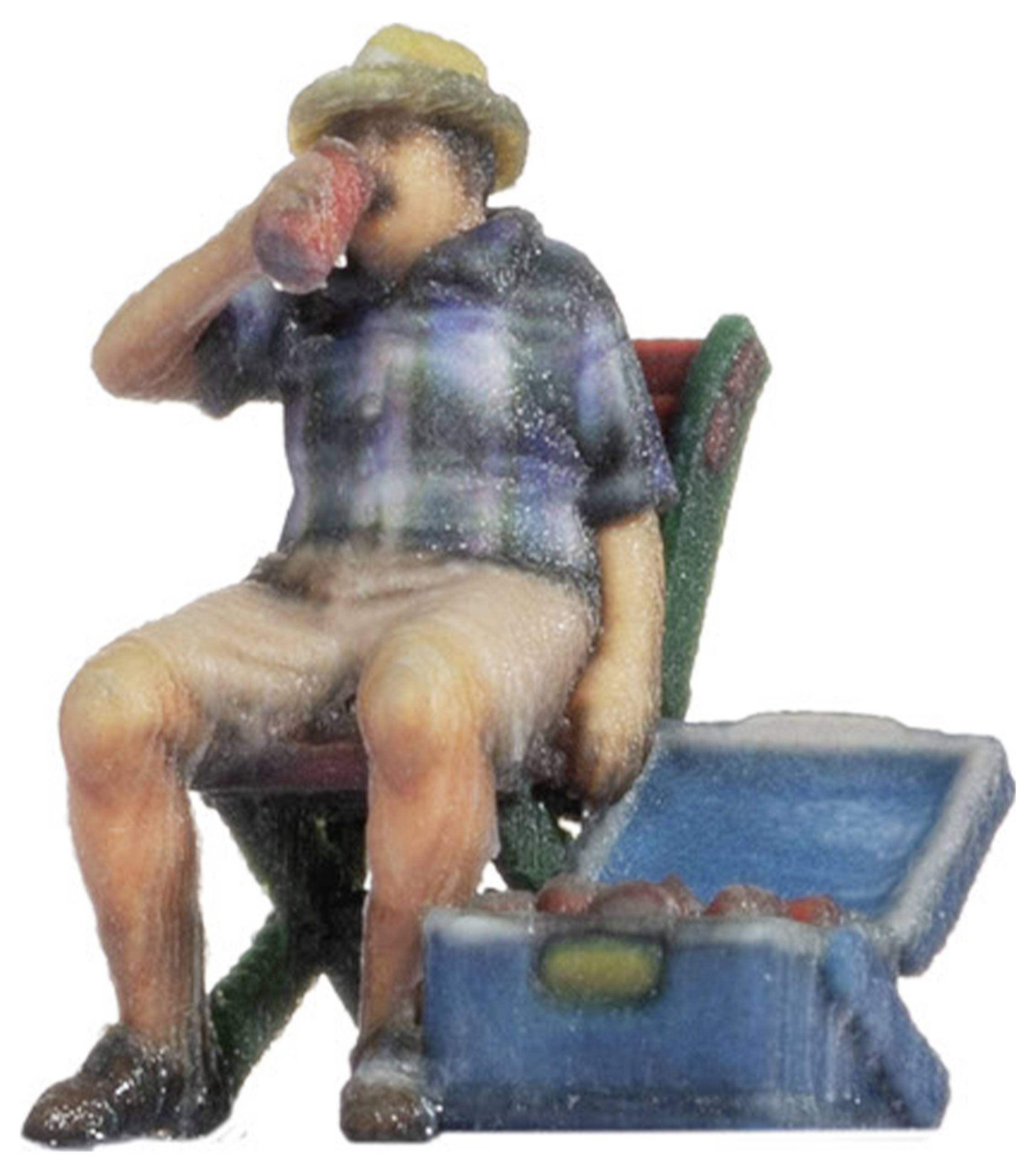 A miniature figurine of a man wearing a straw hat, sitting on a chair and drinking from a tin. Next to him stands an open cool box.