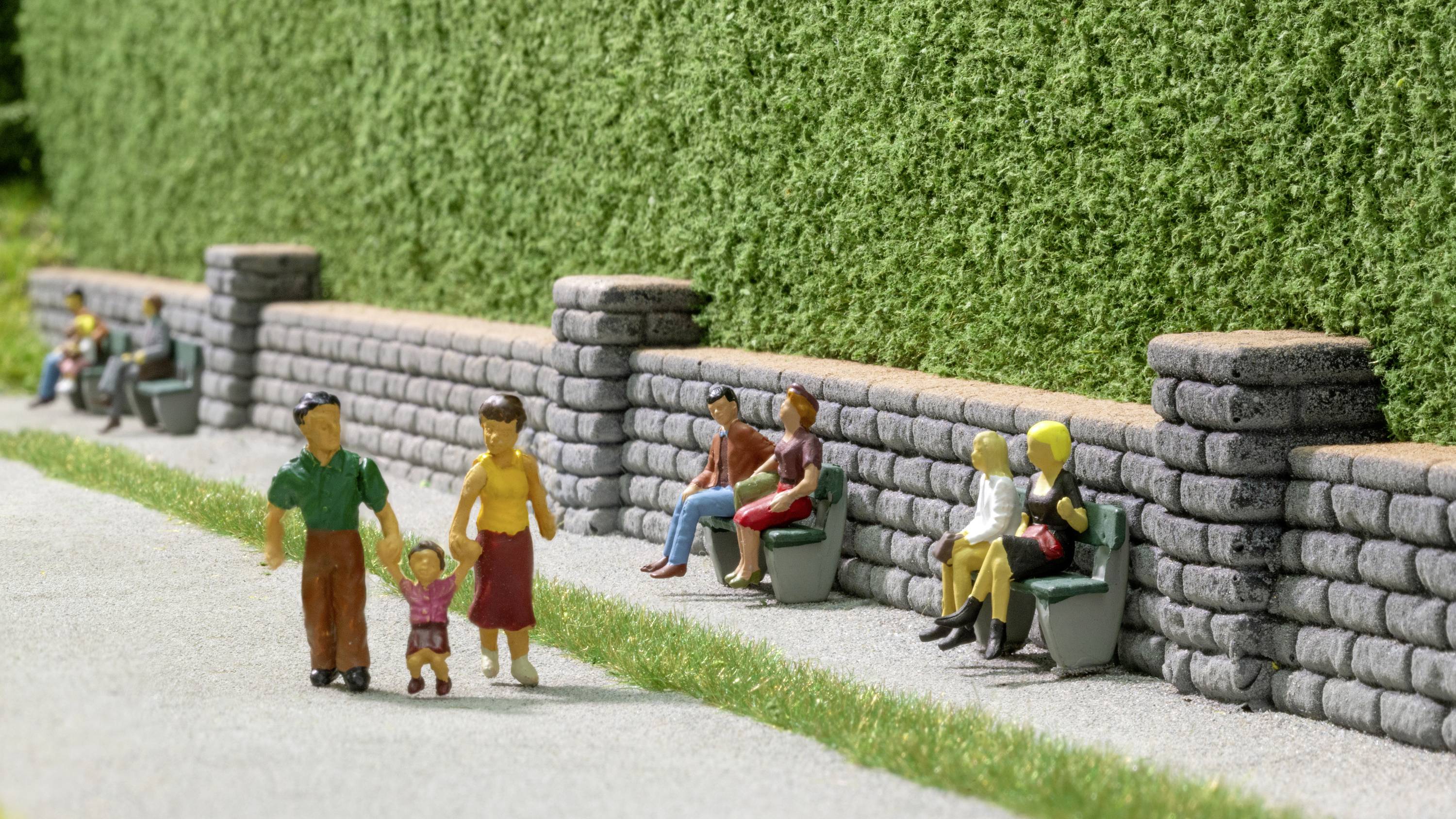 A miniature representation of a park. In the foreground, a family with a small child is walking; in the background, people are sitting on benches.