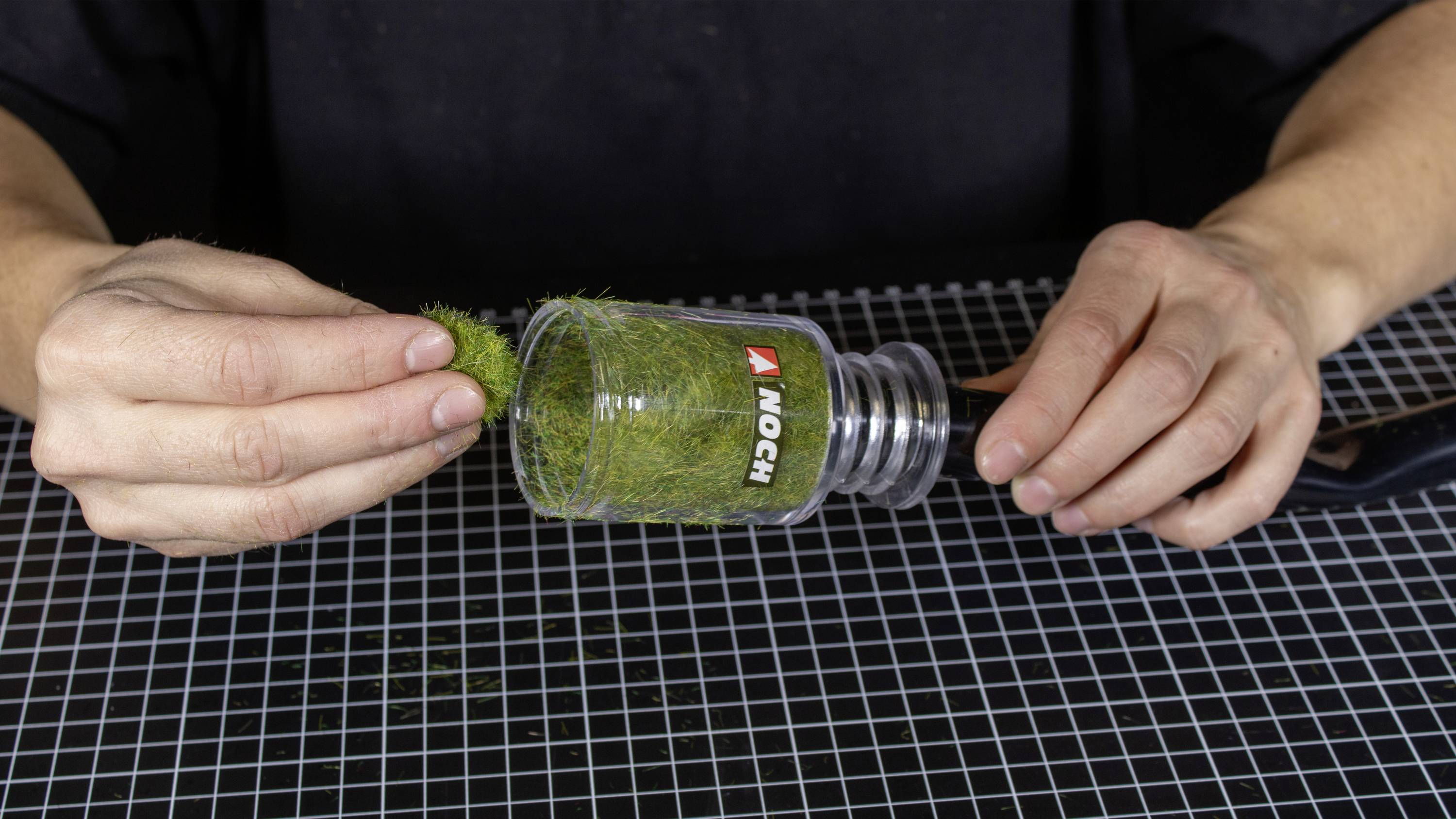 A person is using a static grass applicator tool to apply artificial grass onto a modelled surface.