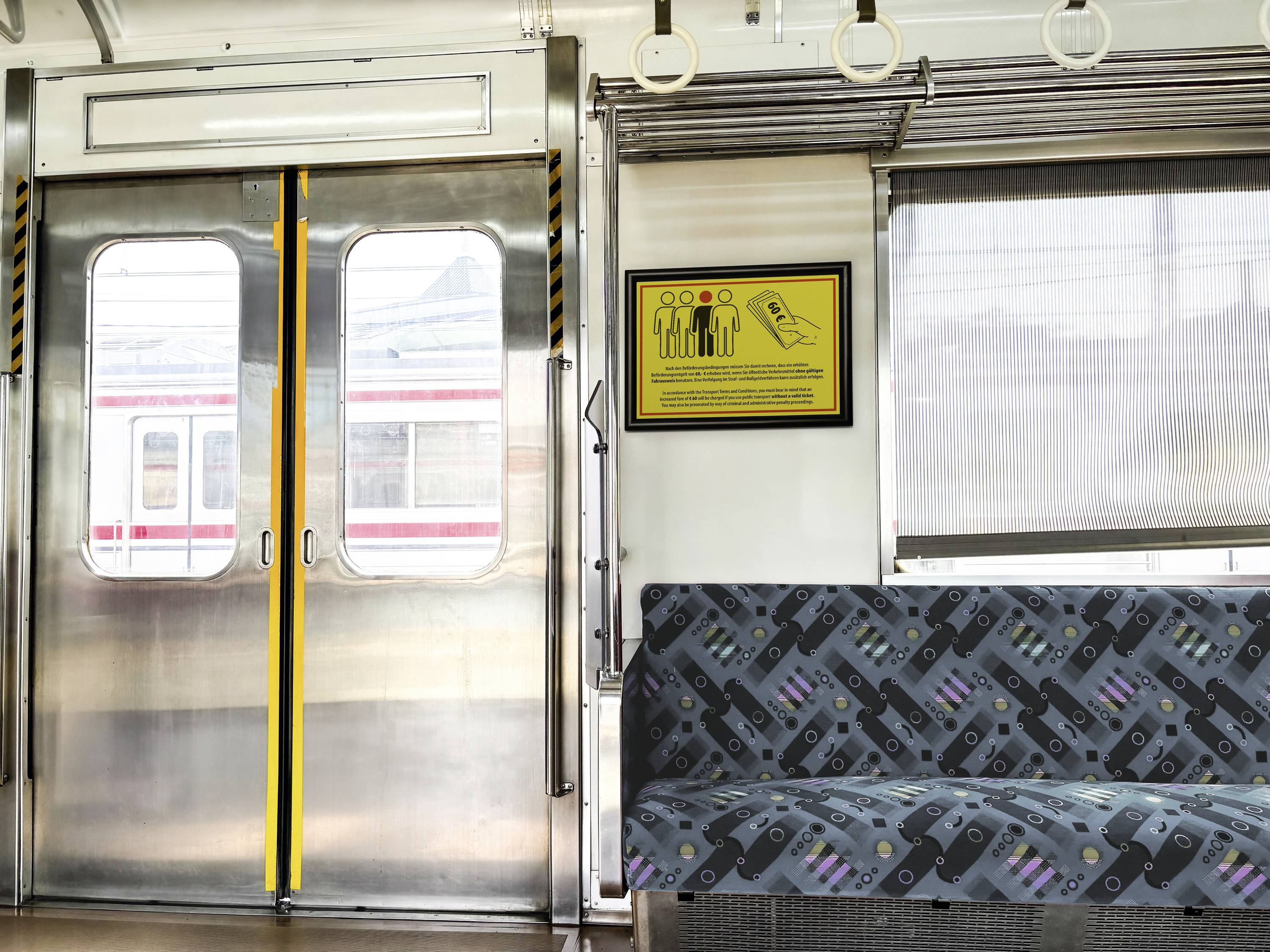 Interior of a train carriage: door, seating arrangement sign, padded bench seat, window overlooking a passing train.