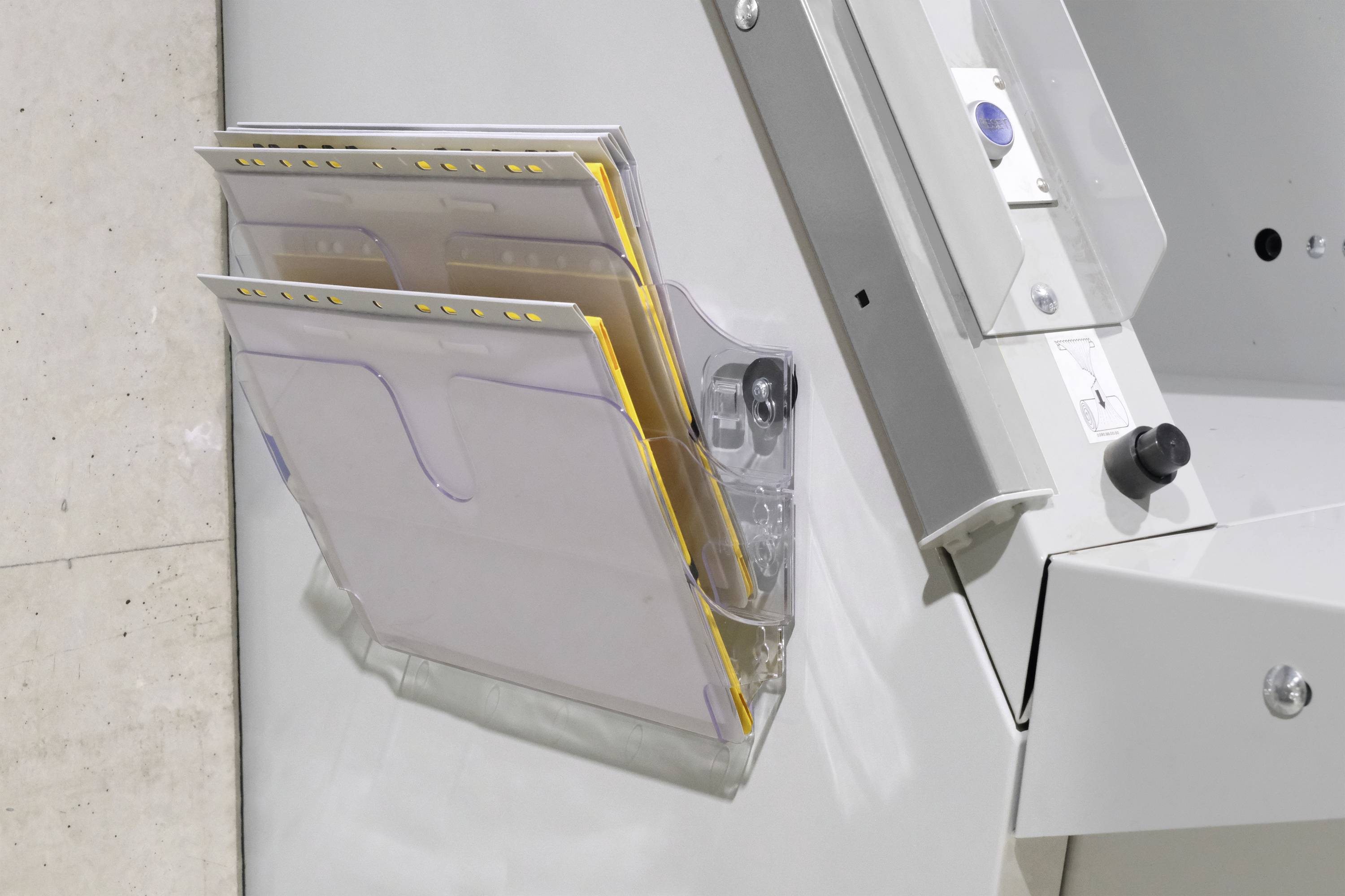 A grey metal container with multiple paper compartments is mounted on the wall. The compartments are partially filled with documents.