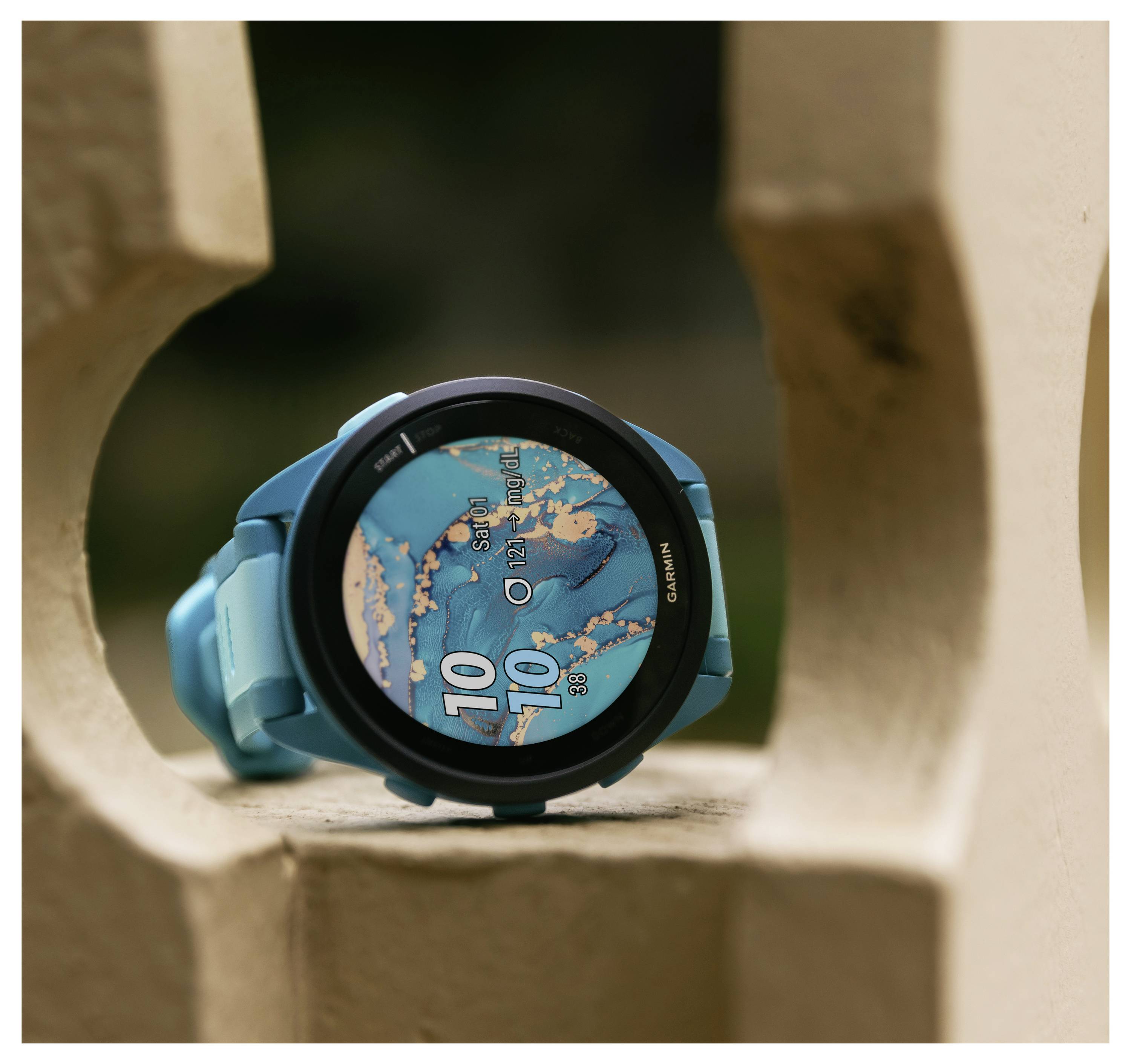 A smartwatch with a blue strap displays the time as 10:10 on a digital watch face. The background is out of focus.