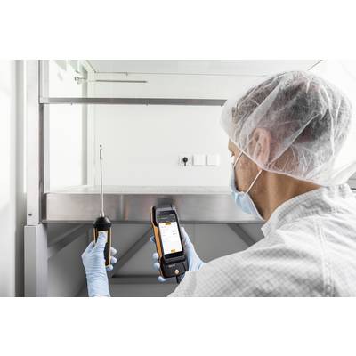 A technician is measuring air quality in a laboratory using a mobile device. He is wearing protective clothing and a hair net.