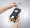A person is holding a measuring device with multiple ports and a hook, ready for installation or use in a technical environment.