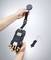 A person is holding an electronic measuring device with multiple ports and a detachable strap. A hook lies beside it.