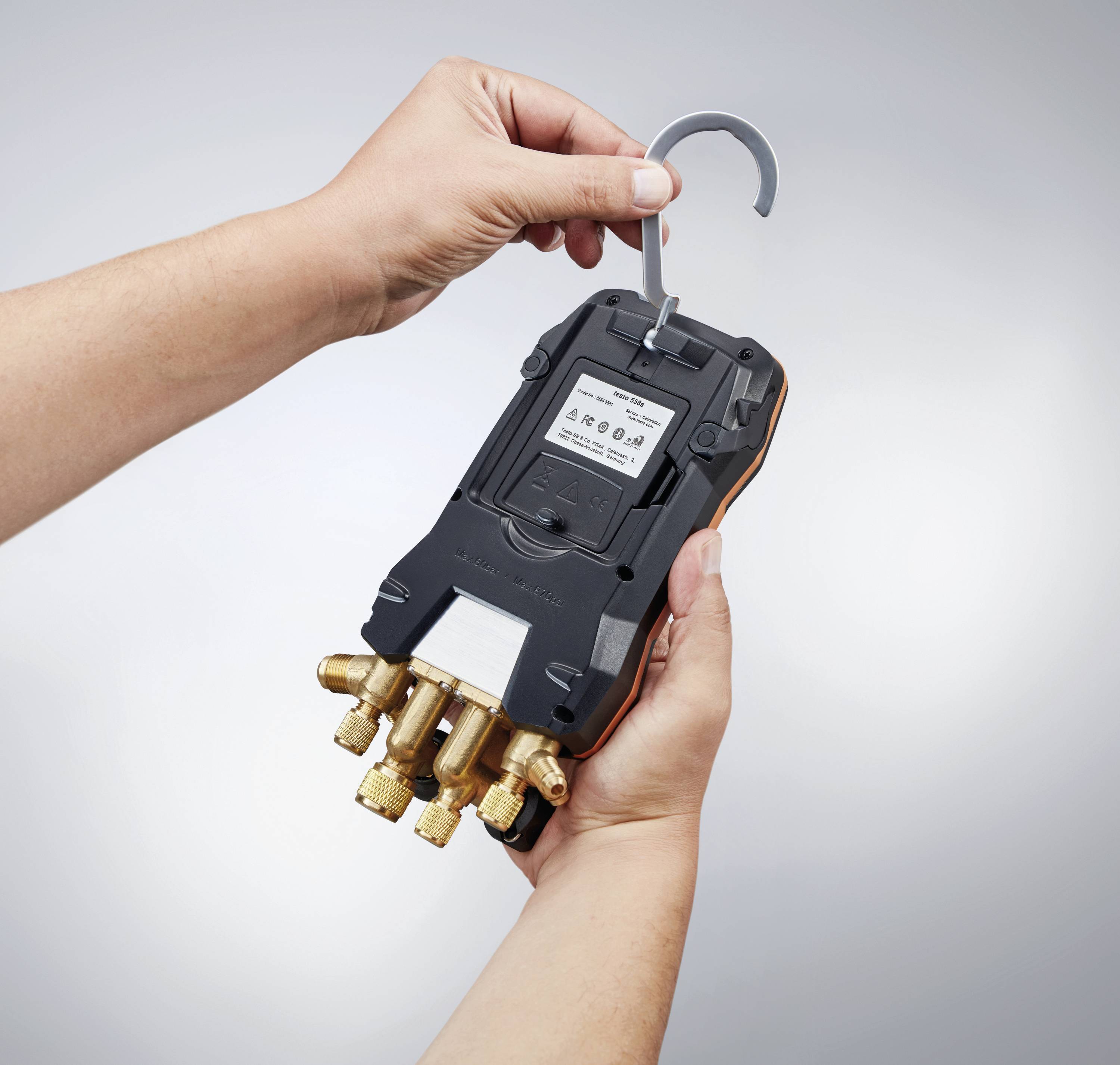 A person is holding a digital pressure gauge with multiple ports, which is attached to a hook.