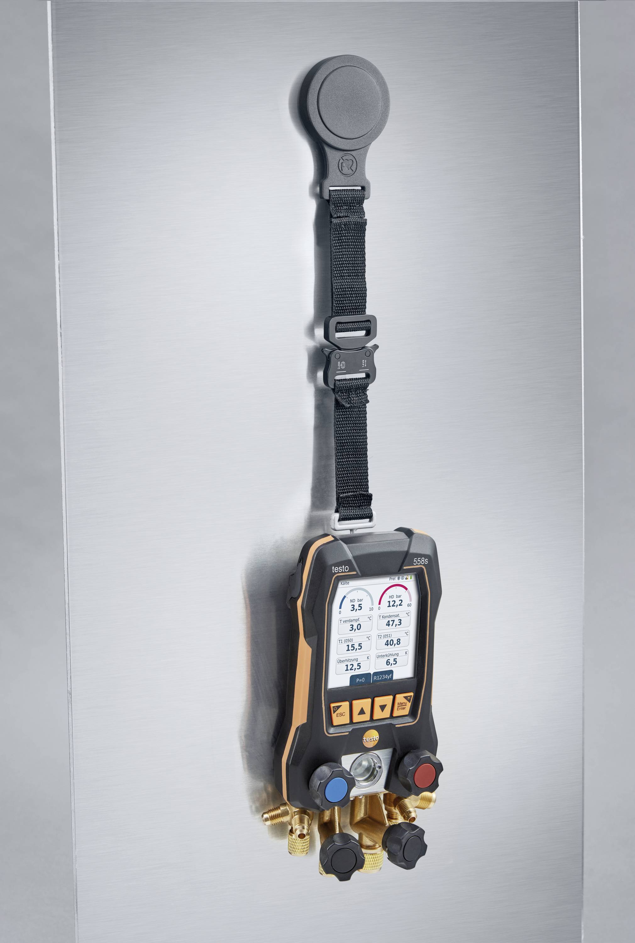 A digital measuring device with multiple ports and colour-coded valves mounted on a metallic surface.