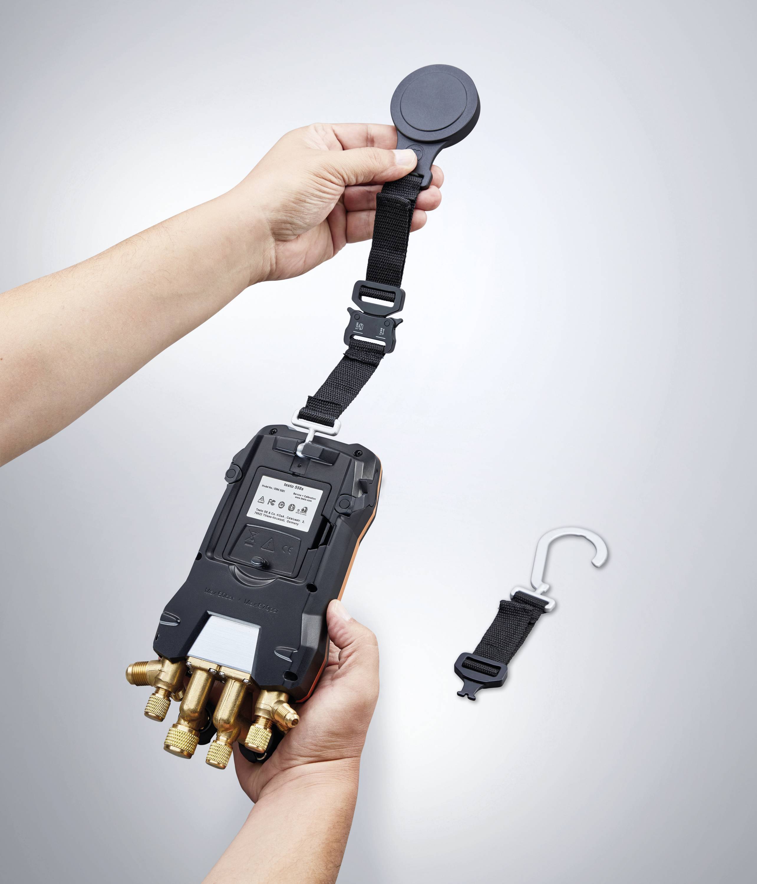 A person is holding a measuring device with multiple ports and a detachable hook in their hand. A strap is being attached.