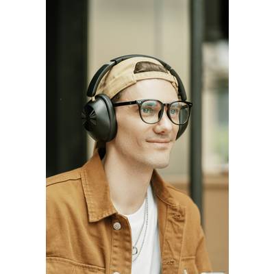 A person wearing glasses and headphones, dressed in a light shirt and brown jacket, sits smiling and looking to the side.