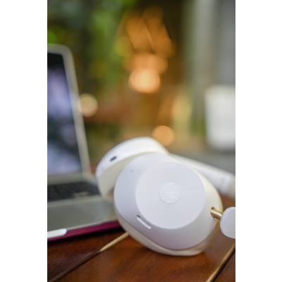 White headphones are lying on a wooden table next to a laptop. The background is blurred and shows colourful lights.