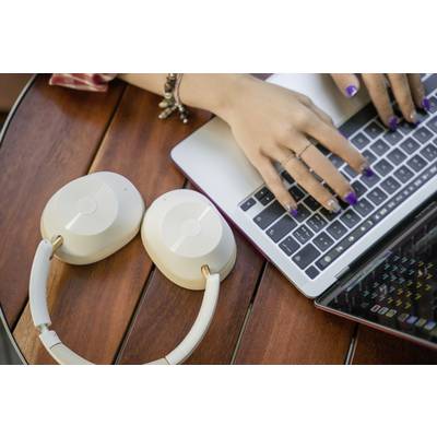 Hands typing on a laptop keyboard, with white headphones lying beside them on a wooden table.
