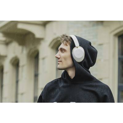 A person wearing a hoodie is listening to music through headphones and looking to the right. Buildings can be seen in the background.