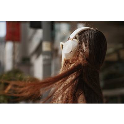 A woman with long, flowing hair is wearing large headphones and walking through an urban environment.