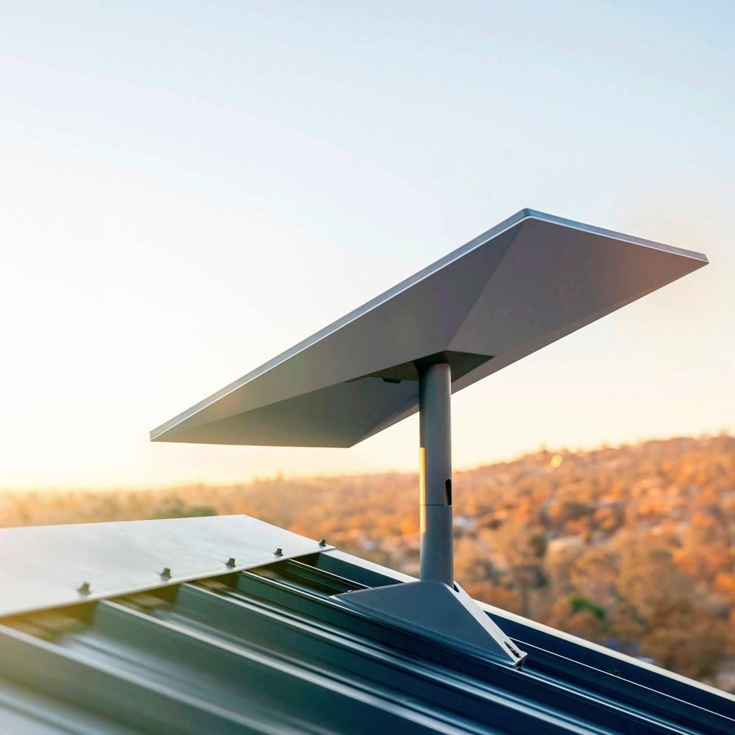 A modern satellite dish on a roof with a background of wooded hills at sunset.