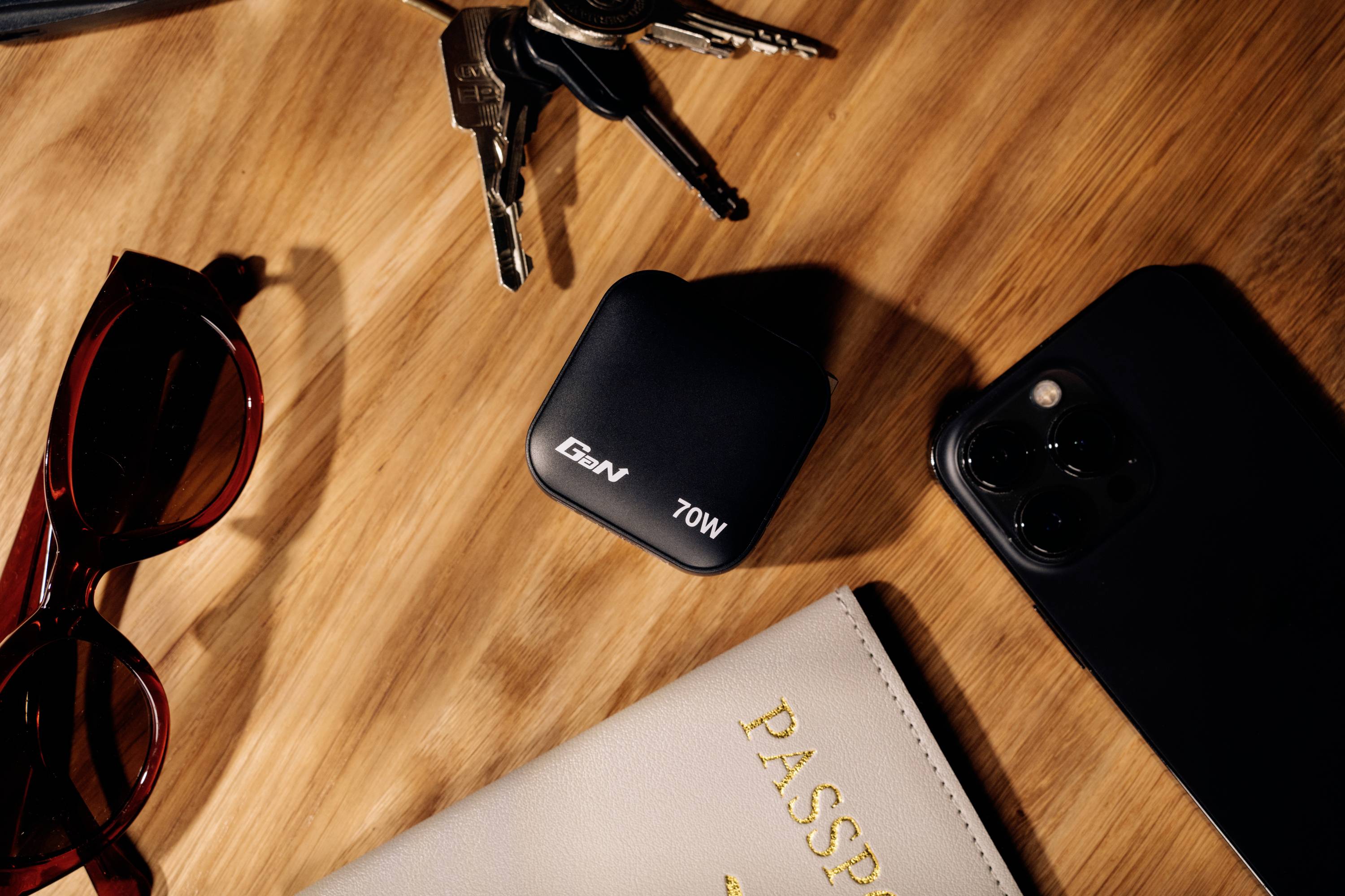 'A desk with sunglasses, keys, a 70W charger, a smartphone and a passport with the inscription 'PASSPORT'.'