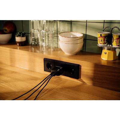 Three black cables are plugged into a socket on a wooden kitchen counter. Beside them are glasses, bowls, and cups.