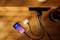 A smartphone and wireless earphones are being charged simultaneously via a wall charger on a wooden table.