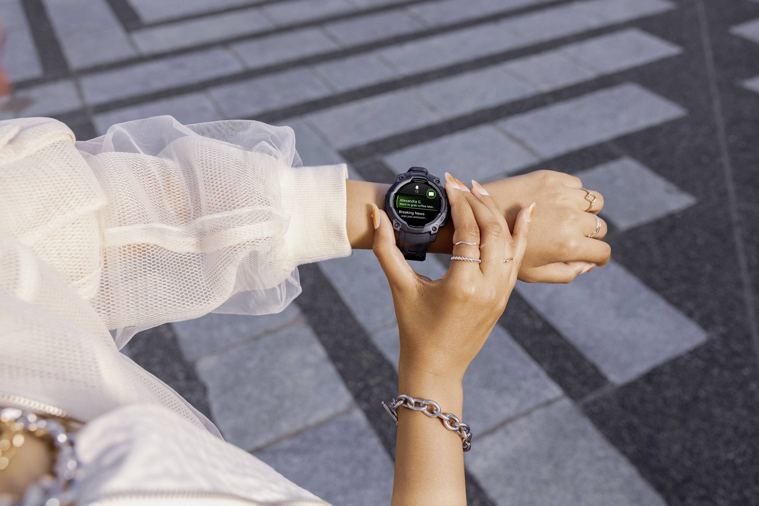 A person is wearing a smartwatch and reading a notification on the display while walking on a paved path outdoors.