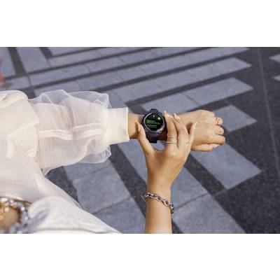A person is wearing a smartwatch and reading a notification on the display while walking on a paved path outdoors.