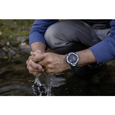 A person kneels by a river and collects water with their hands. They are wearing a wristwatch with a red display.