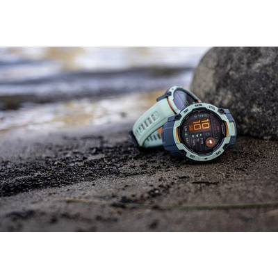 Two sporty wristwatches are lying on a rocky beach. The dial of one watch shows the numeral '10'. Water is visible in the background.