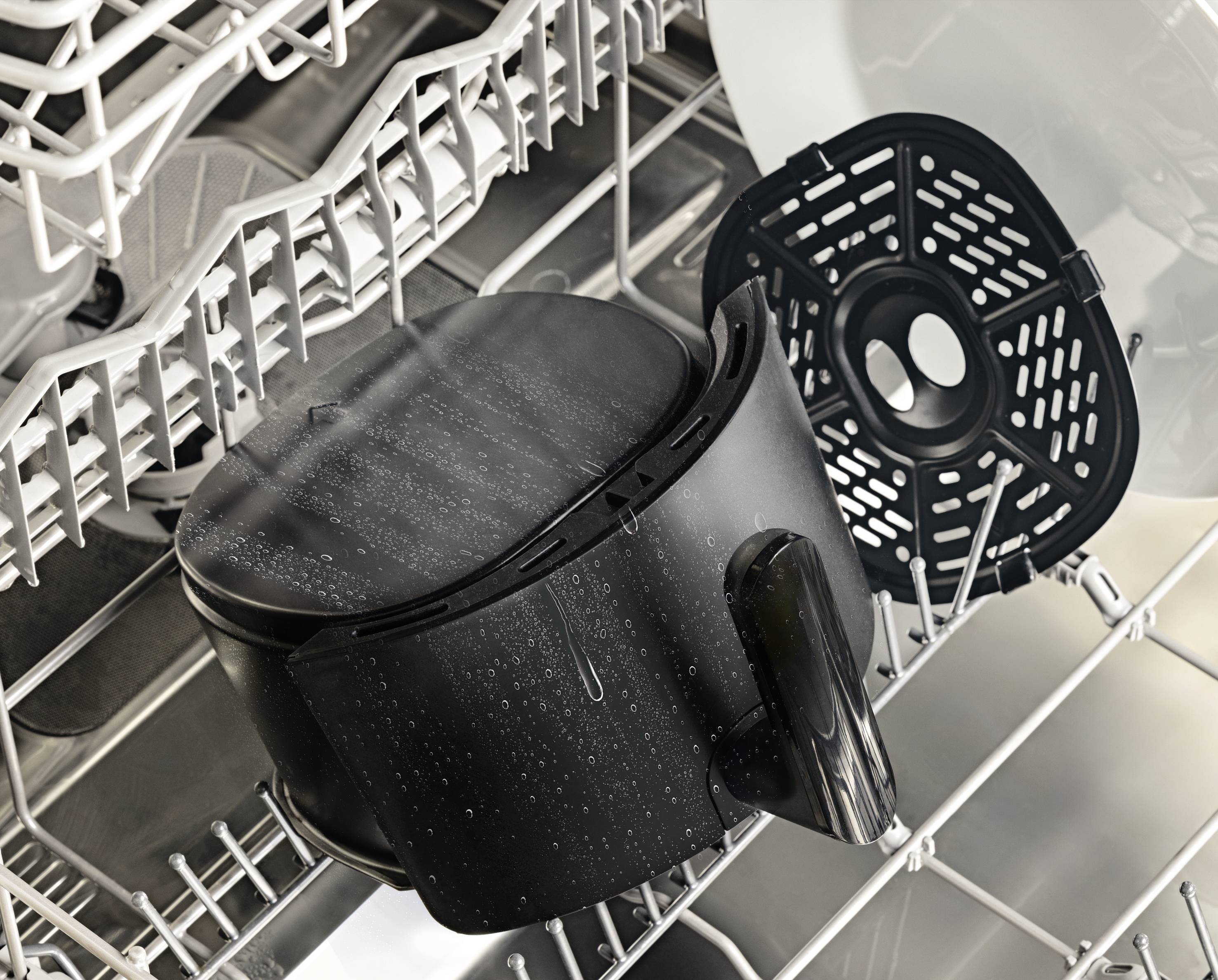 A black air fryer container and a removable filter basket are being cleaned in the top rack of a dishwasher.