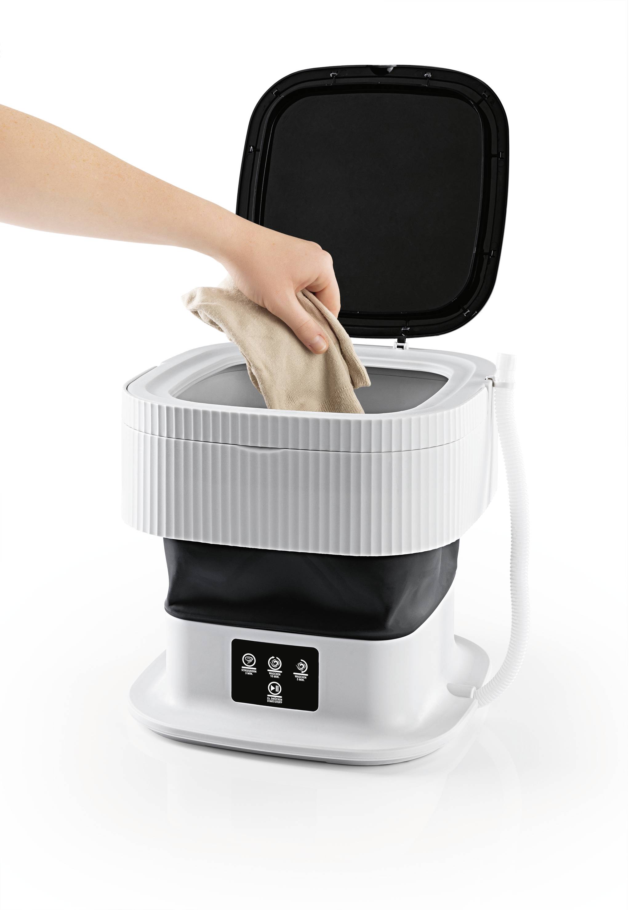 A person is placing a garment into a portable mini washing machine with an open lid. The machine is white with black elements.