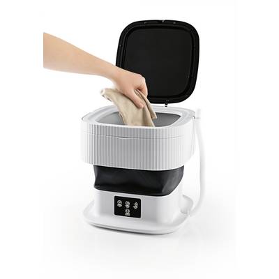 A person is placing a garment into a portable mini washing machine with an open lid. The machine is white with black elements.