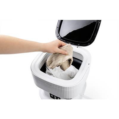 A hand places a garment into a compact, open washing machine. It demonstrates the simple loading and user-friendliness.