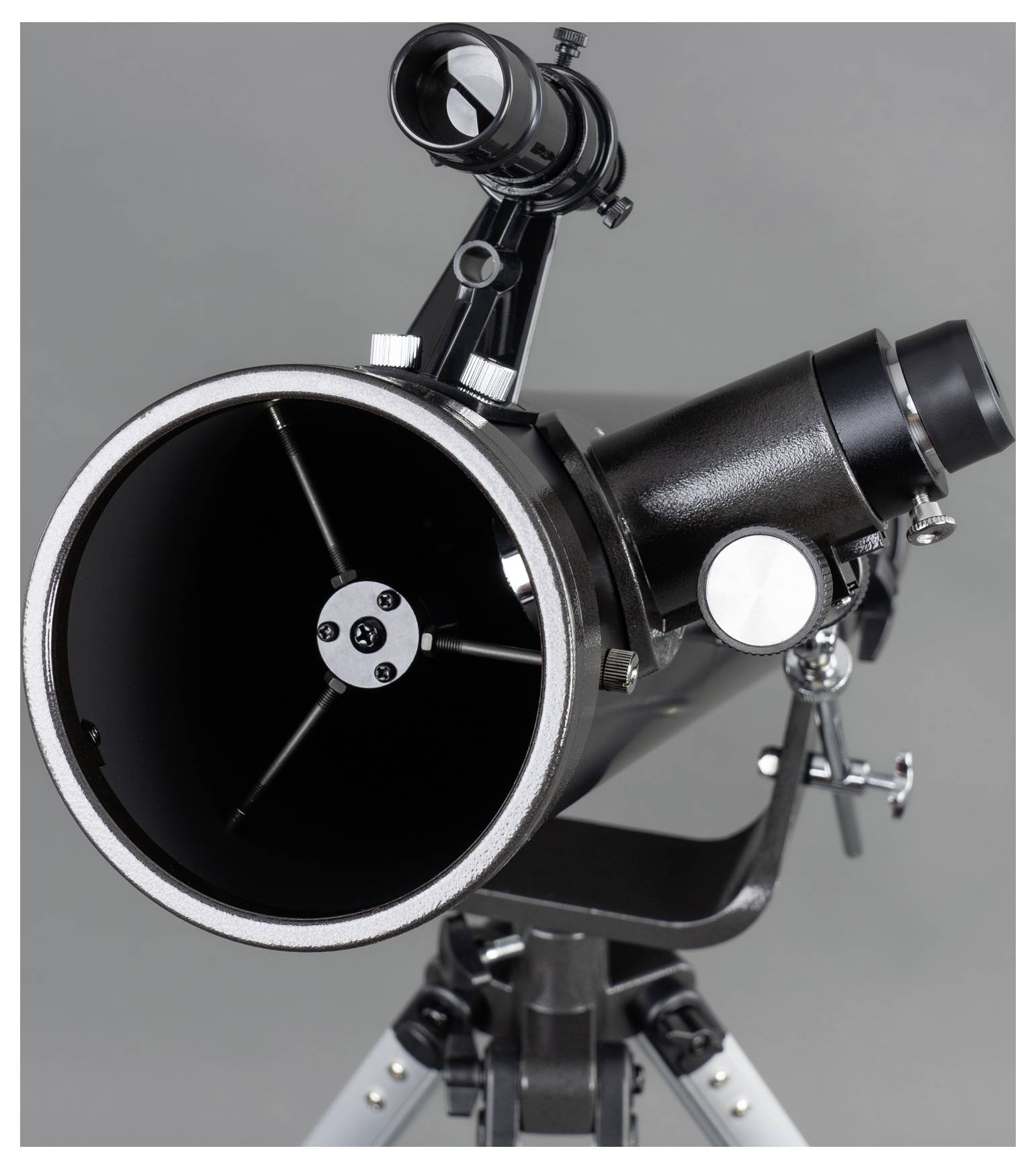 A black telescope with a tripod is pictured against a grey background. It has a large main tube and a smaller finder scope.