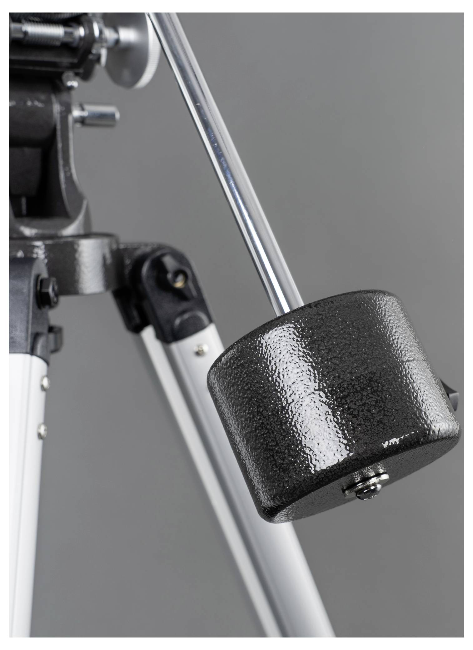 A telescope tripod with a large, black counterweight on a metal rod. The tripod is standing against a grey background.