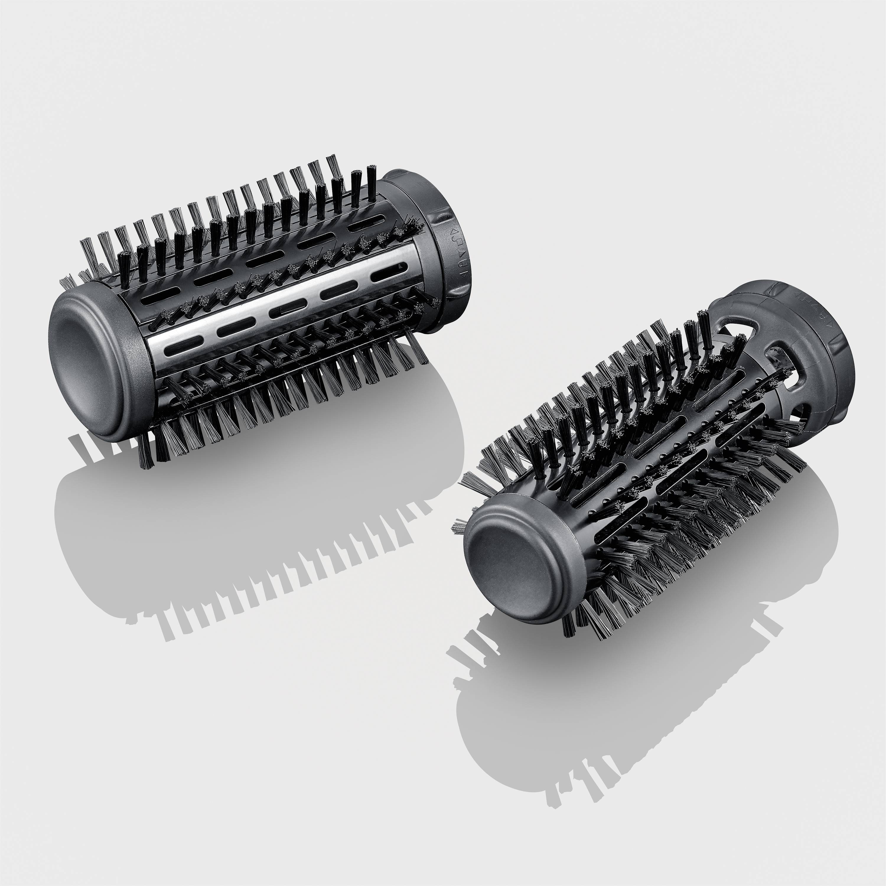Two black round brushes with bristles, reflecting on a grey surface. Suitable for hair styling devices.