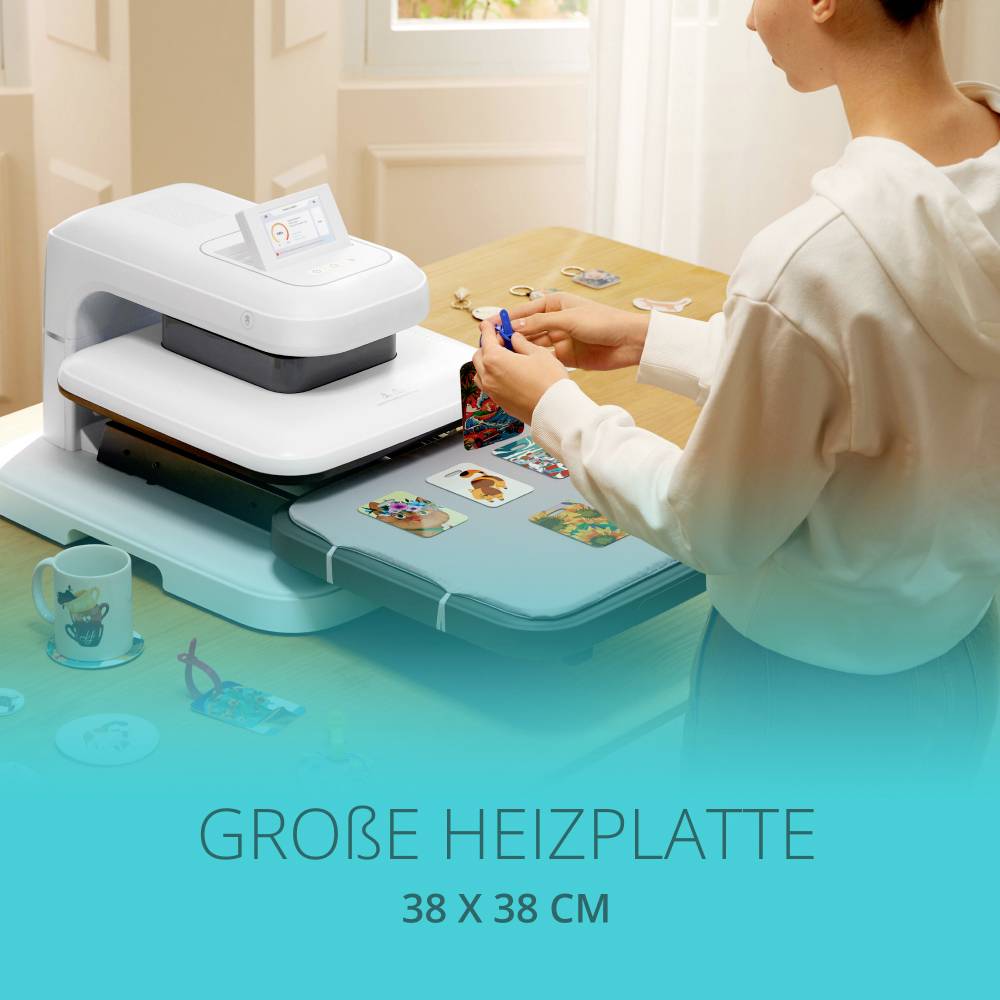 A person is using a textile finishing device with a large heating plate (38 x 38 cm) on T-shirts. A cup is sitting next to it on the table.