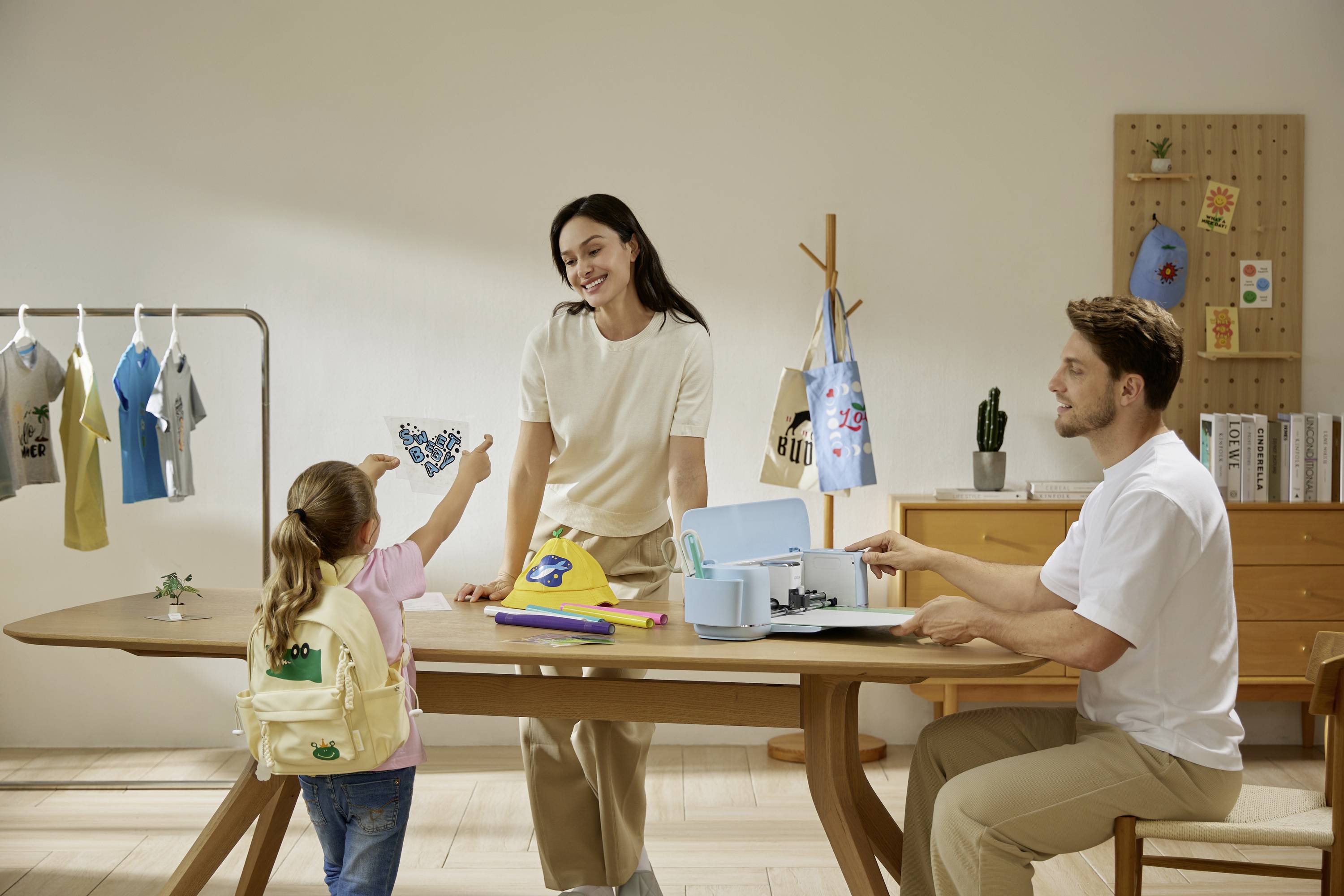 A family crafts together in a creative space. A child proudly shows a handmade object, while the parents smile and help.