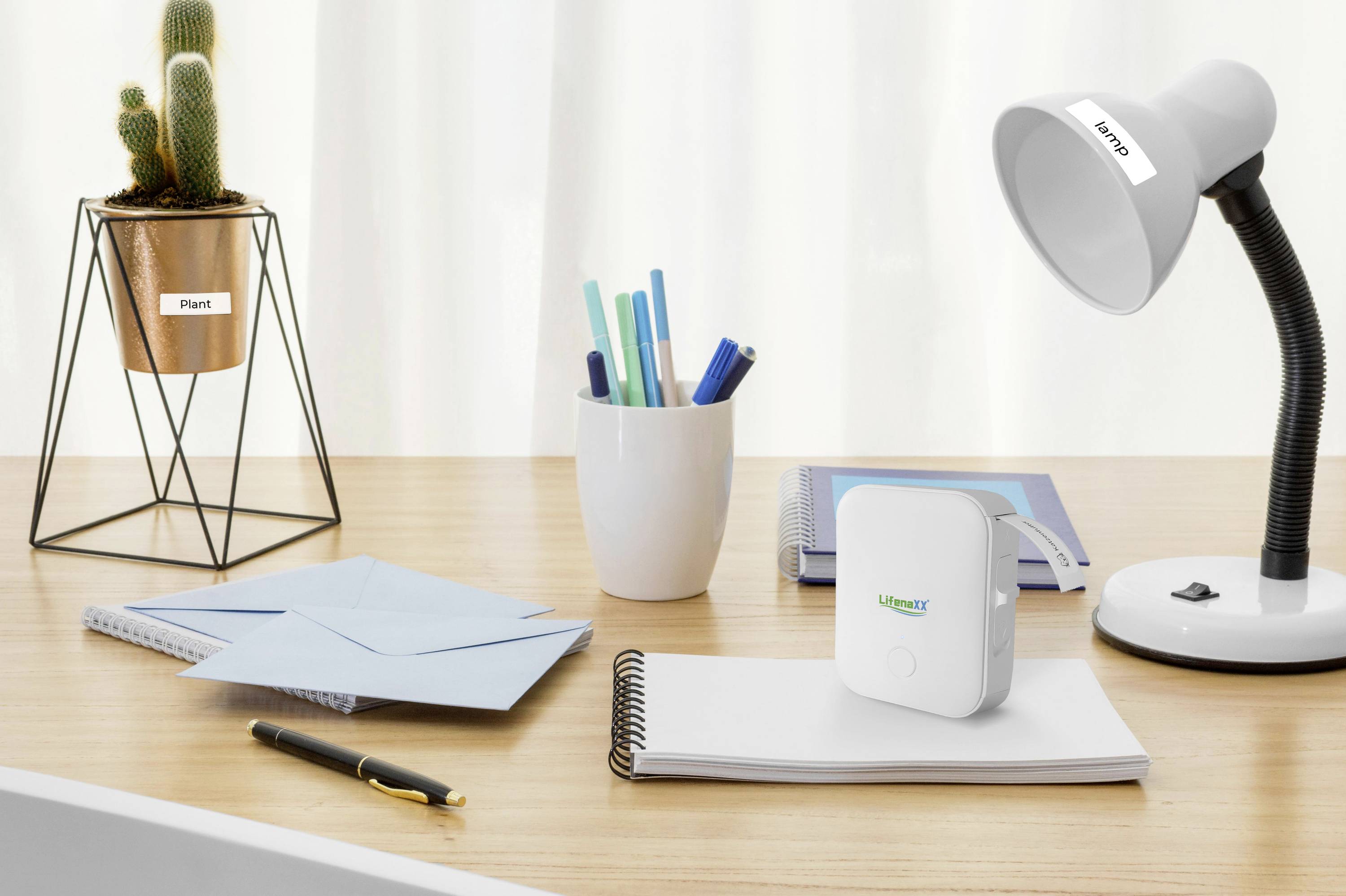 Desk with potted plant, lamp with 'Lumen' label, pens in a cup, and notepad. Focus on a small, square device.