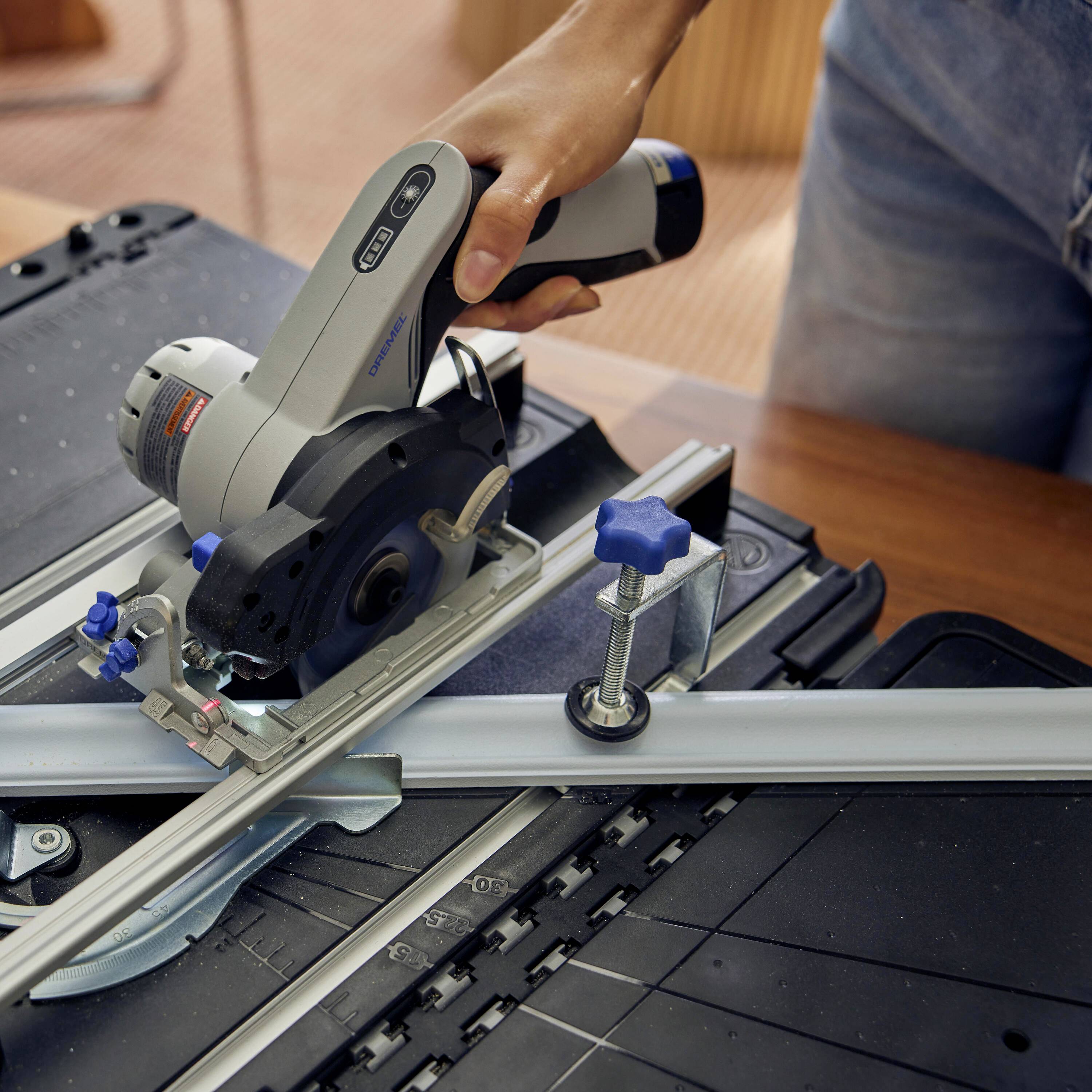 A person is using a handheld circular saw to cut a piece of wood. The saw is equipped with a guide rail.