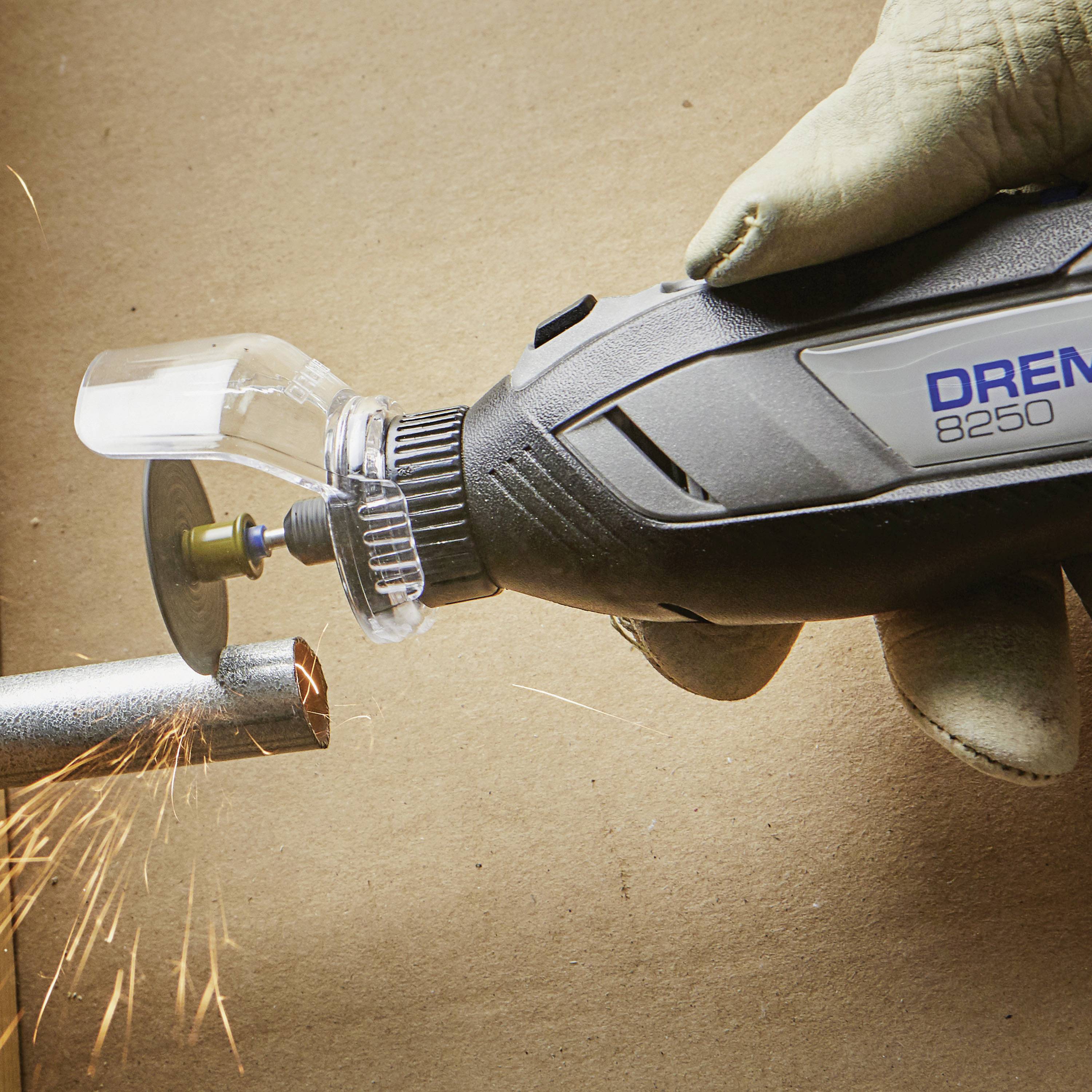 A hand wearing a glove is holding a Dremel tool 8250 while cutting metal. Sparks are flying from the point of contact.