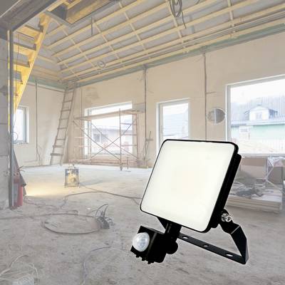A construction site in an unfinished room with a ladder, scaffolding, and a bright work light on the floor.